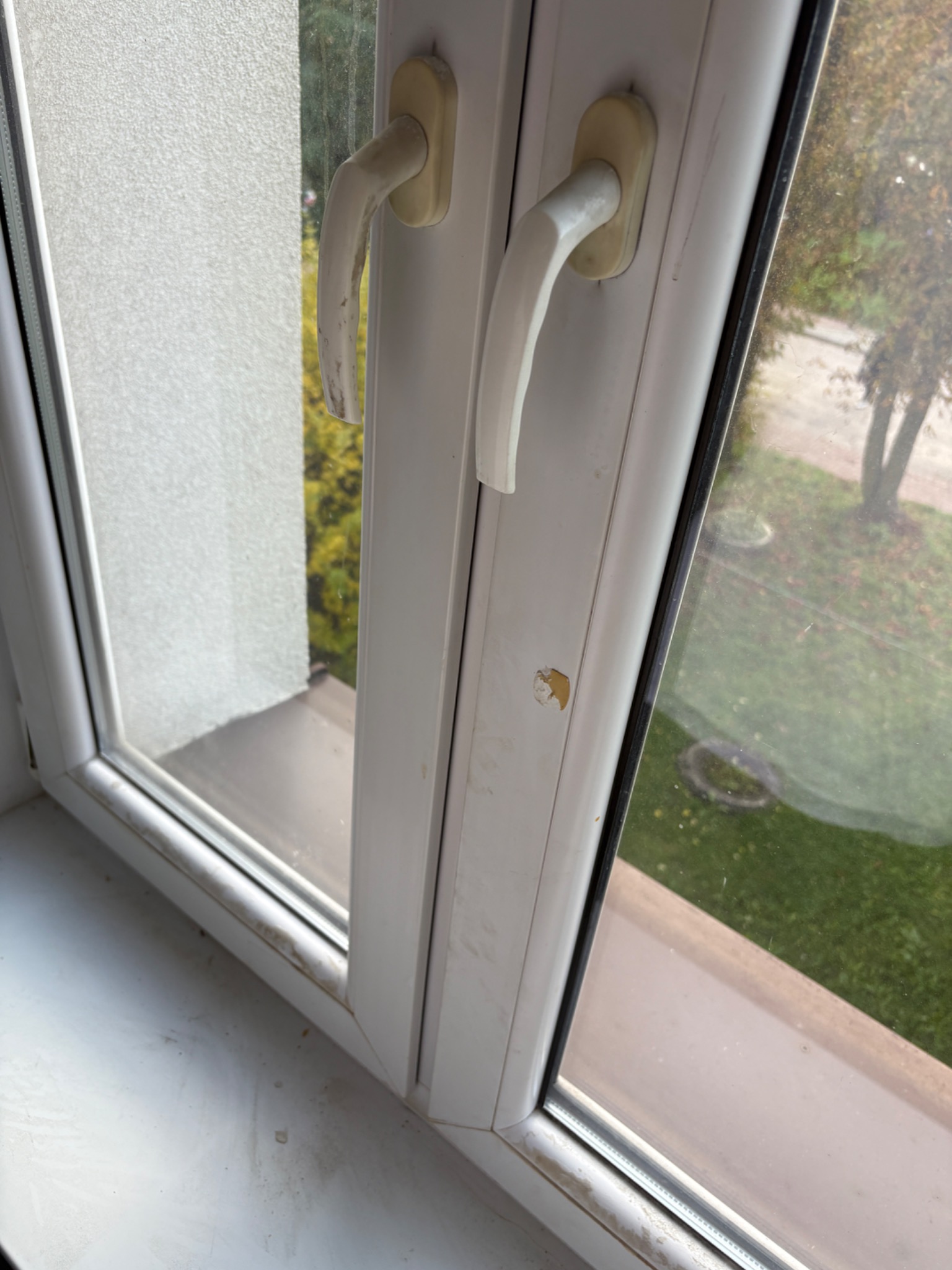 Brudne okno PCV z widocznymi smugami i osadami na szybie oraz ramie. Widoczne zabrudzenia na parapecie i uszkodzenia na ramie okiennej.