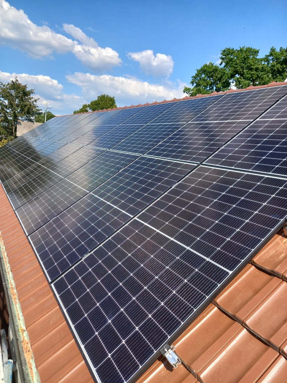 Panele słoneczne zamontowane na brązowym dachu w Krosno Odrzańskie, widok z dołu, błękitne niebo z chmurami w tle.