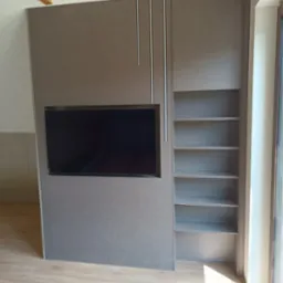 Szara zabudowa meblowa z wnęką na telewizor i regałem na książki, widoczne drewniane belki sufitowe i parkiet na podłodze.