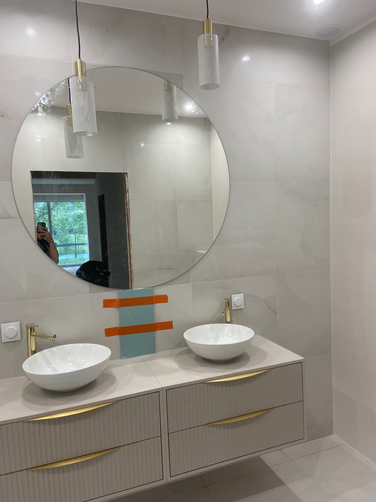 Wykończona łazienka w Nowym Dworze Mazowieckim: białe umywalki nablatowe, złote baterie, duże okrągłe lustro i płytki imitujące marmur. Nowoczesny design.