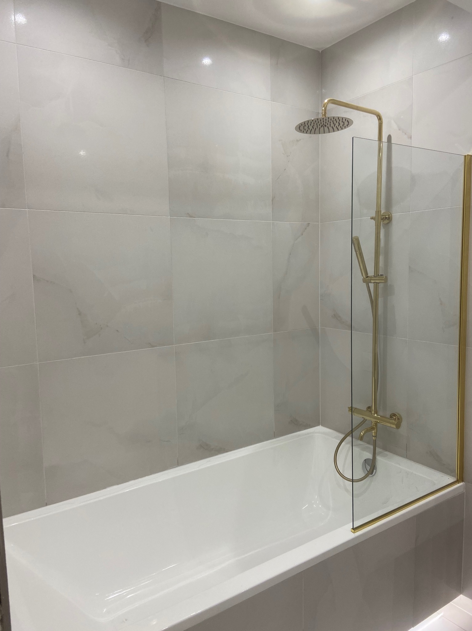 Wykończona łazienka z wanną, szklanym parawanem i złotą armaturą. Płytki imitujące marmur na ścianach. Nowoczesny design.