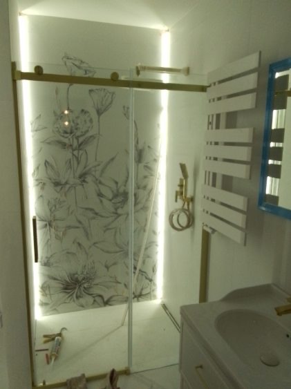 Nowoczesna kabina prysznicowa z przesuwnymi drzwiami, zdobiona motywem kwiatowym, podświetlona LED, z elementami armatury w kolorze złotym i białym grzejnikiem.