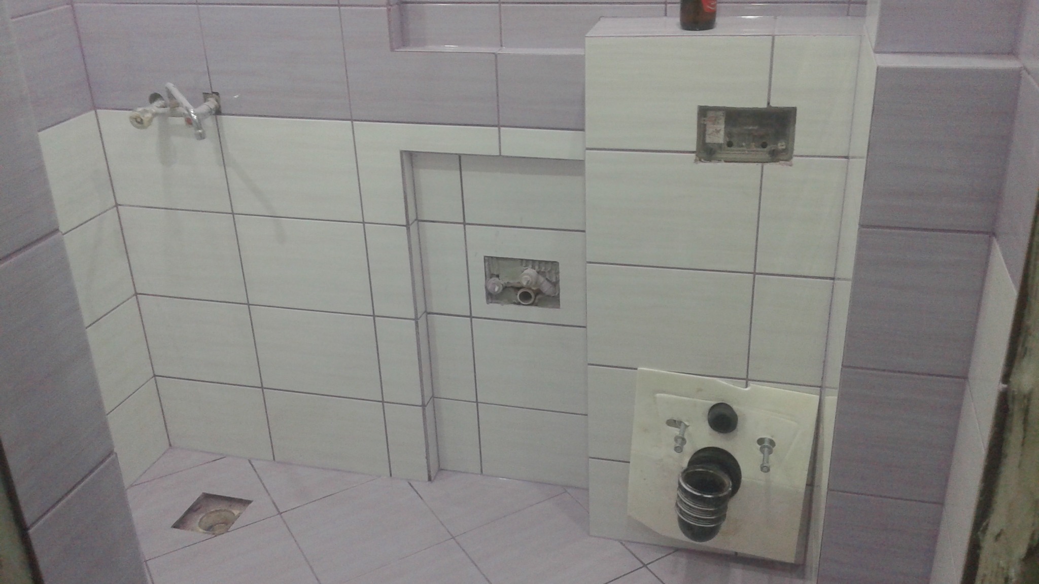 Łazienka w trakcie remontu: biało-szare płytki, widoczne instalacje wodno-kanalizacyjne przed zabudową, przygotowane miejsce na armaturę.