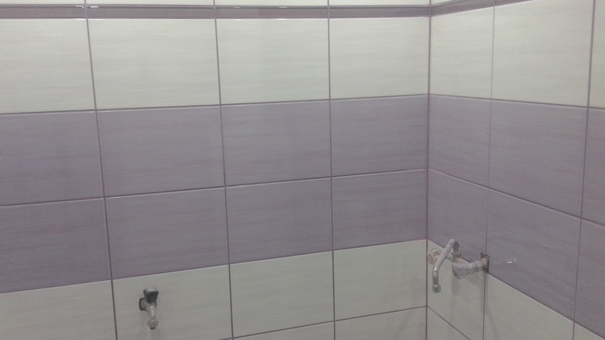 Wykończona łazienka z dwukolorowymi, ułożonymi płytkami w odcieniach szarości i bieli. Widoczne baterie umywalkowe. Minimalistyczny design.