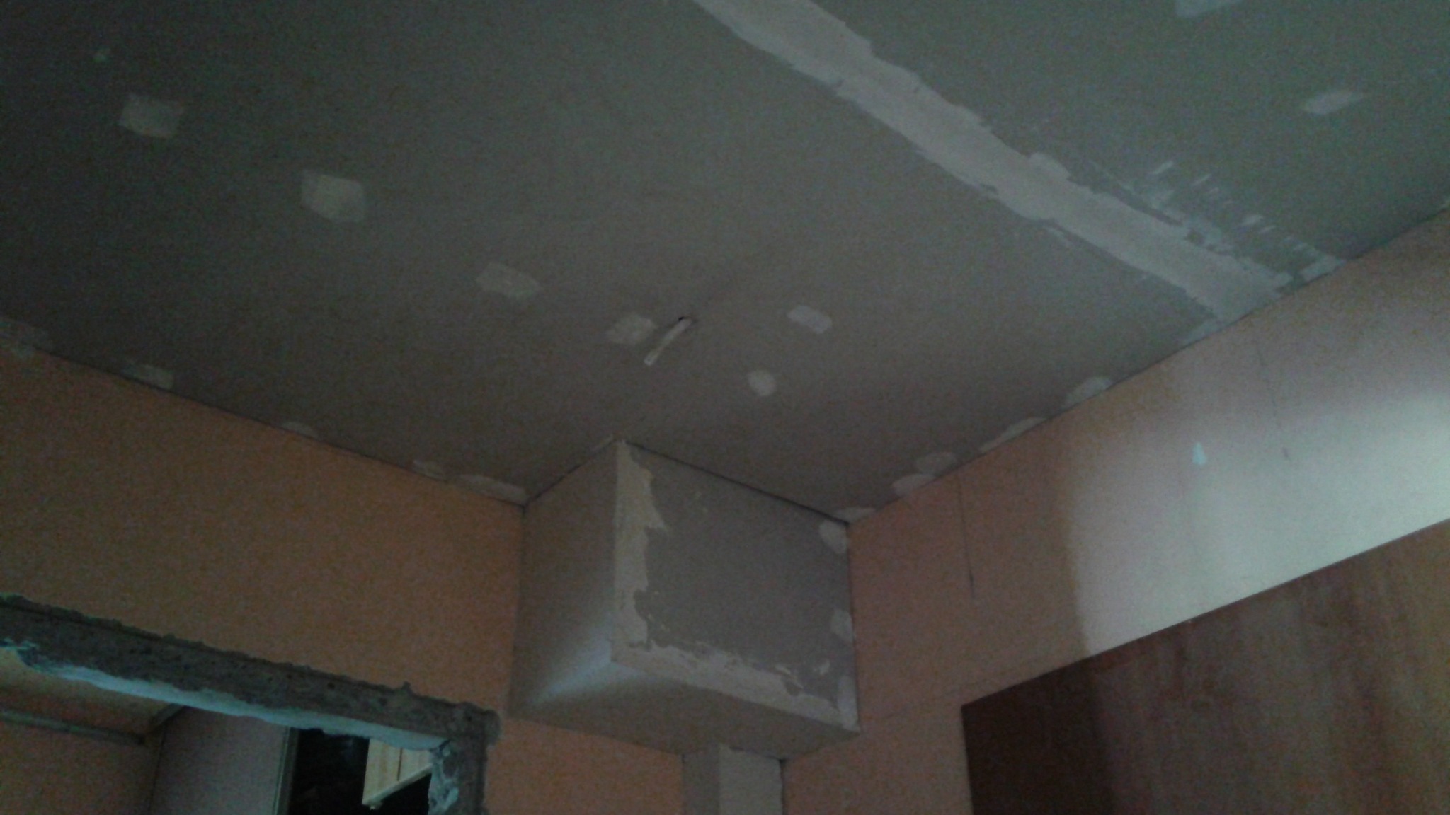 Narożne ujęcie sufitu z płyt gipsowo-kartonowych w trakcie szpachlowania, widoczne łączenia i fragmenty ścian w pomieszczeniu. Prace wykończeniowe wewnątrz budynku.