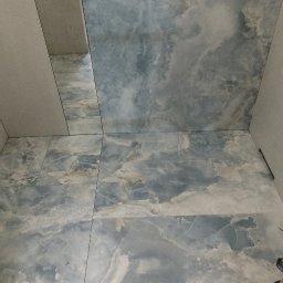 AlexBud - Niebiesko-białe płytki imitujące marmur na ścianie i podłodze w łazience, widok z dołu, fragment grzejnika na ścianie.