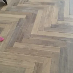 Parkiet ułożony we wzór jodełki francuskiej, widoczna szpachelka i gąbka podczas prac wykończeniowych.