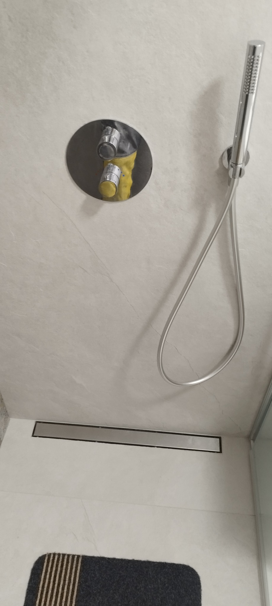 Świeżo wykończona kabina prysznicowa z chromowaną armaturą, deszczownicą i odpływem liniowym; zabezpieczone elementy przed zabrudzeniem w trakcie prac.