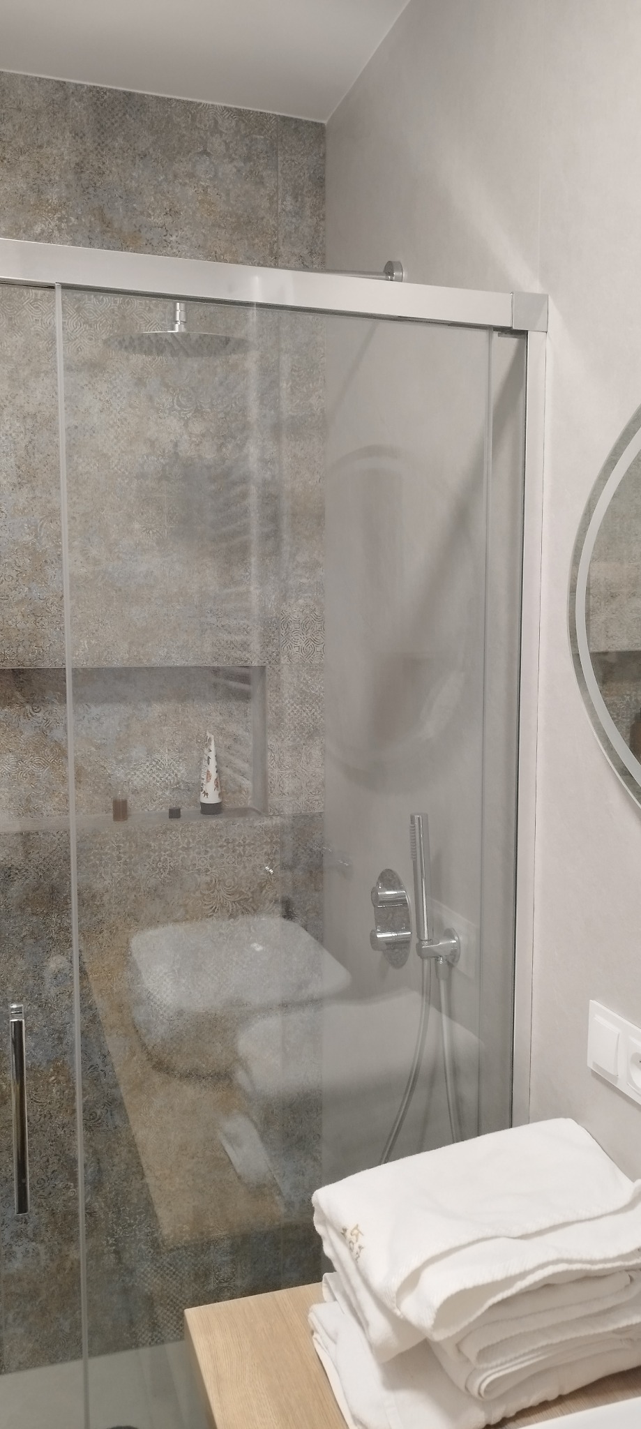 Szklana kabina prysznicowa z deszczownicą i szarymi płytkami w łazience w Wojcieszowie, obok umywalki leżą białe ręczniki.