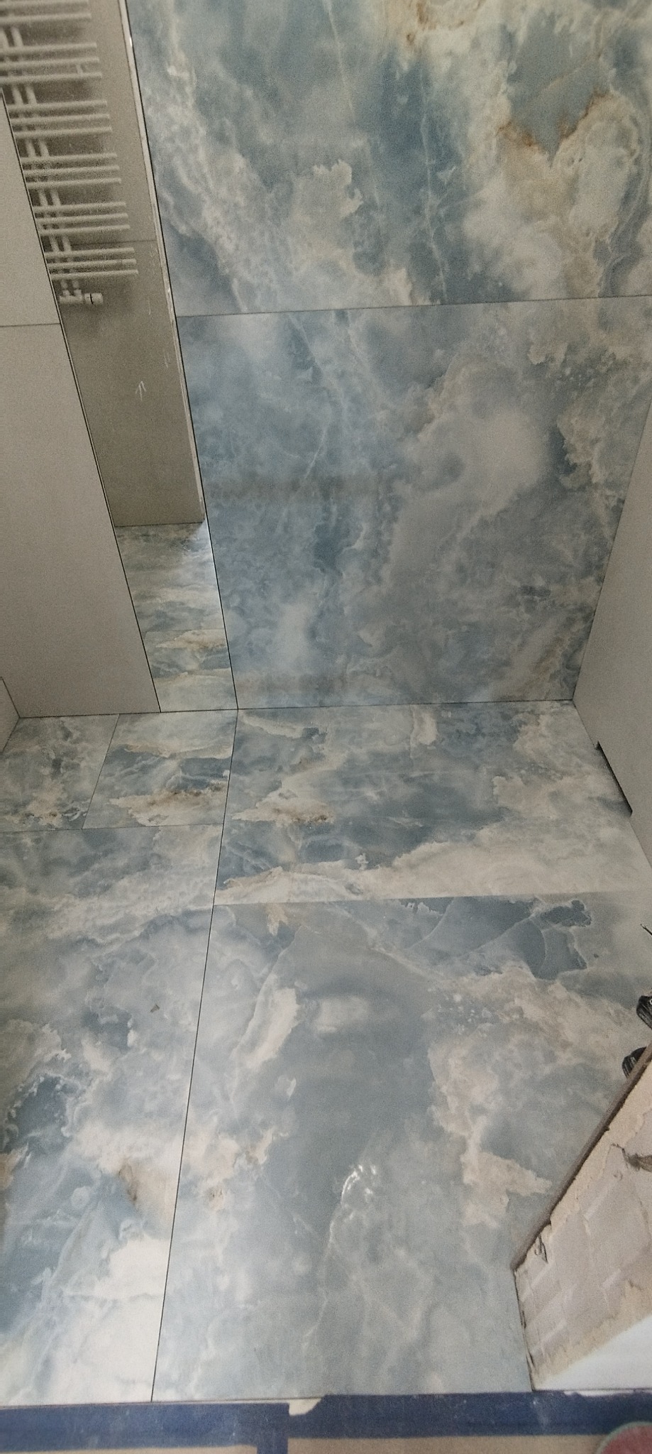 Niebiesko-białe płytki imitujące marmur na ścianie i podłodze w łazience, widok z dołu, fragment grzejnika na ścianie.