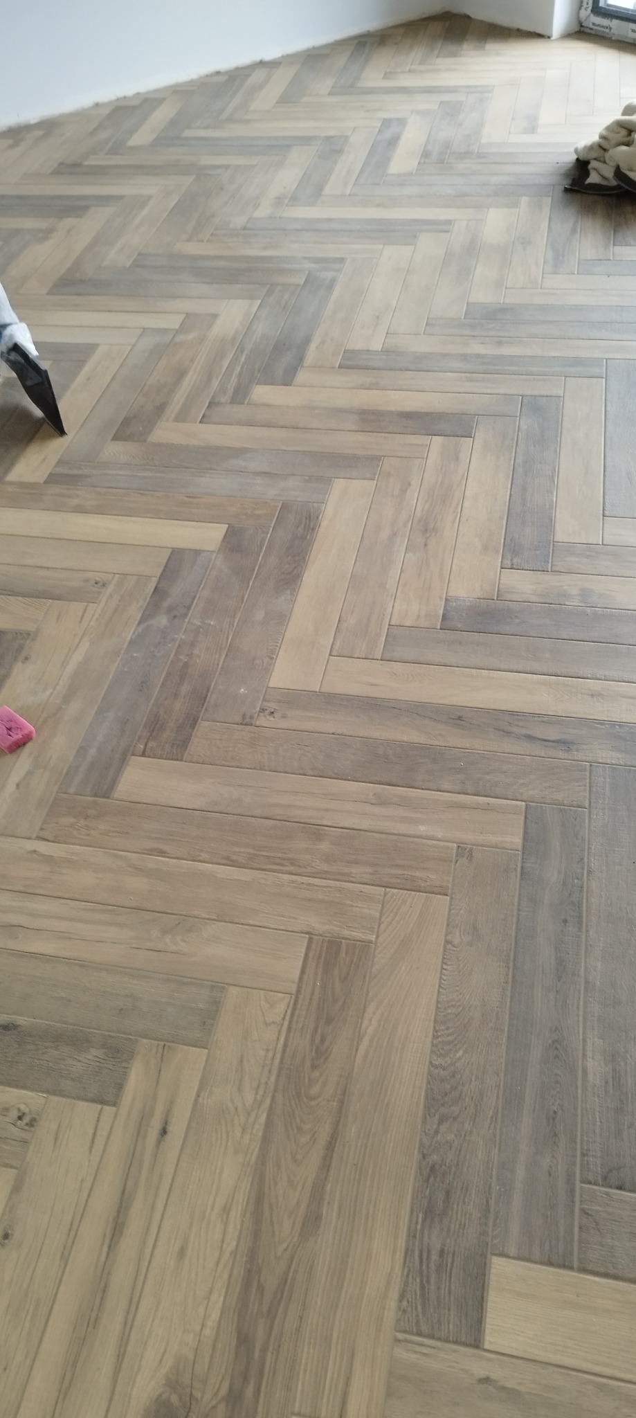 Parkiet ułożony we wzór jodełki francuskiej, widoczna szpachelka i gąbka podczas prac wykończeniowych.