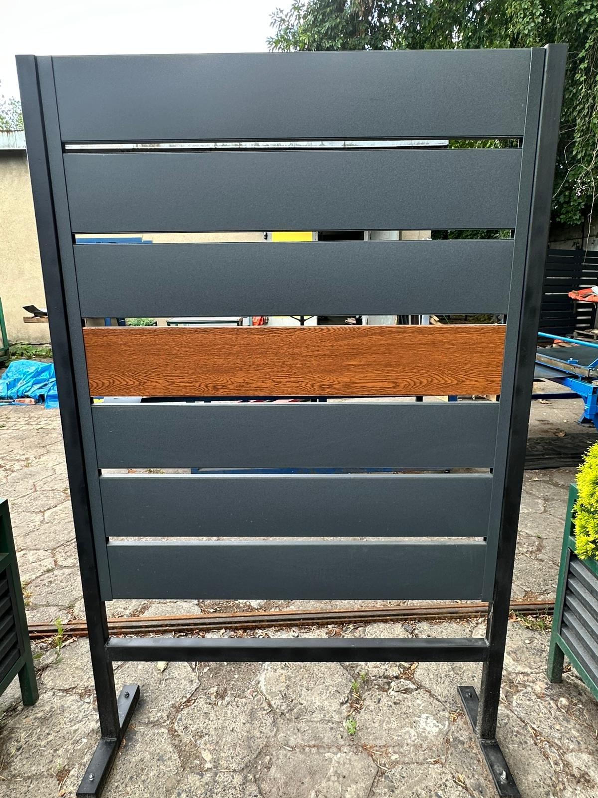 Nowoczesne ogrodzenie panelowe w Krakowie z elementami imitującymi drewno. Szare panele z poziomymi szczeblami i czarną ramą.