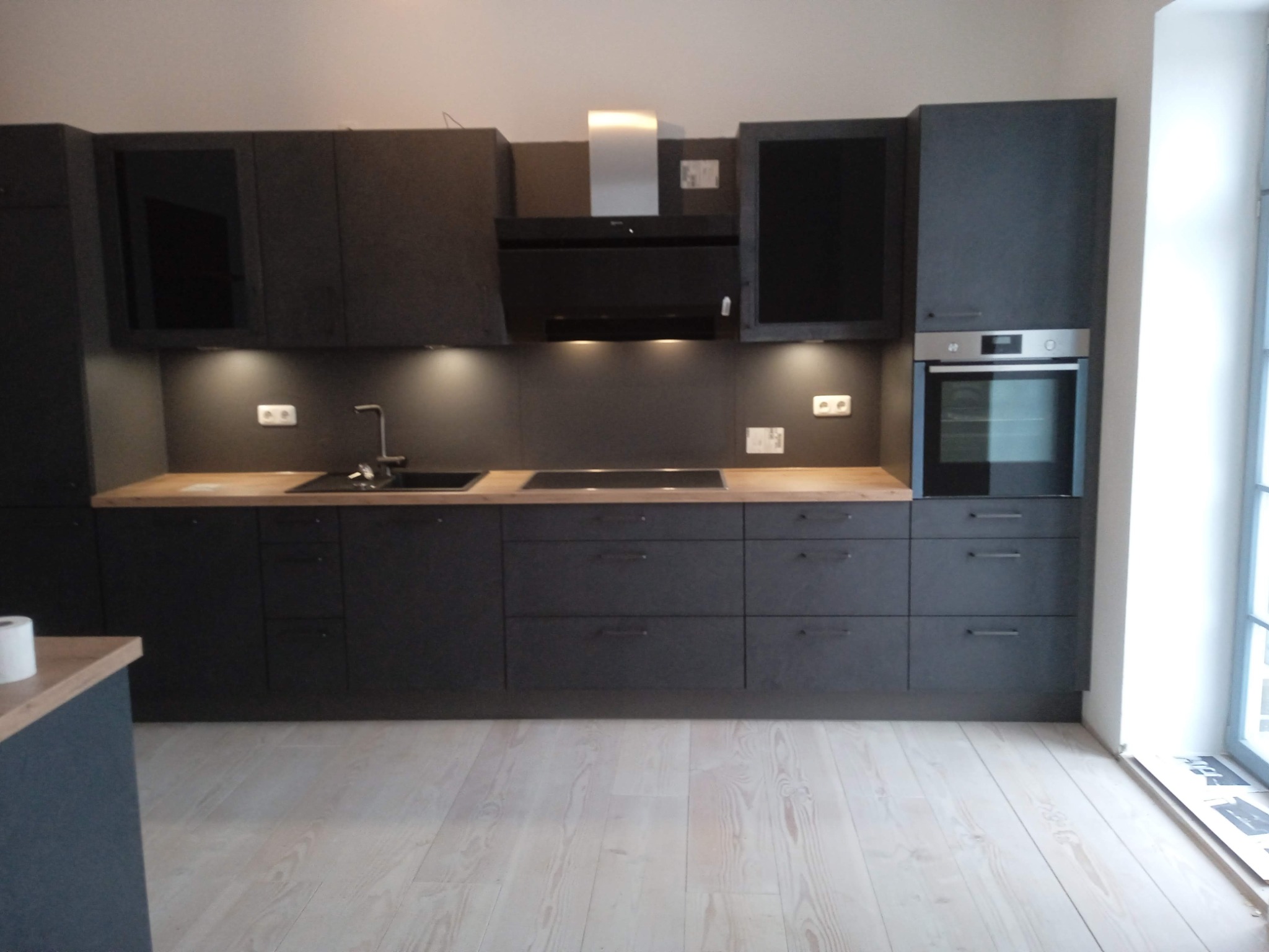 Ciemna, nowoczesna kuchnia z drewnianym blatem i oświetleniem podszafkowym, widok na całą zabudowę z perspektywy podłogi.