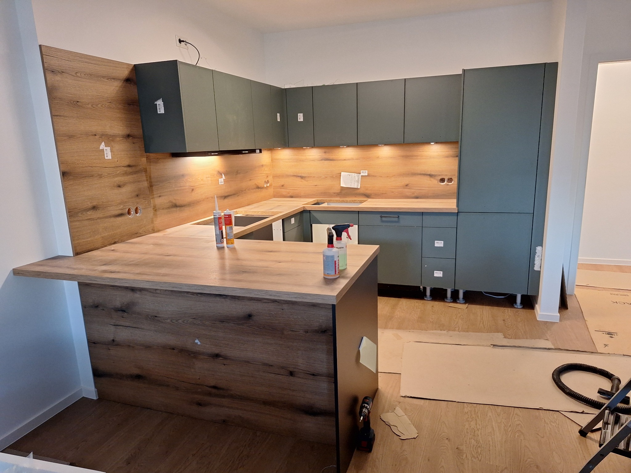 Montaż kuchni z drewnianym blatem i szarymi szafkami. Widoczne narzędzia i materiały montażowe, co sugeruje etap wykończeniowy.