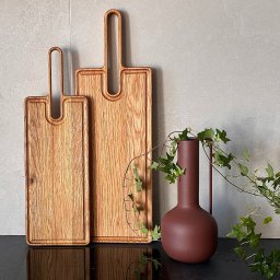 Maeva Home Staging - Dwie drewniane deski do krojenia z uchwytami obok wazonu z bluszczem na czarnym blacie, na tle szarej ściany. Minimalistyczna aranżacja.