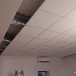 Anatolii Kardynal - Biały sufit podwieszany kasetonowy z widoczną konstrukcją nośną w jednym miejscu, klimatyzator na ścianie, drabina w rogu. Ujęcie z dołu.