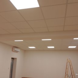 Anatolii Kardynal - Zakończony montaż sufitu podwieszanego kasetonowego z oświetleniem w jasnym pomieszczeniu. Widoczna drabina malarska i klimatyzator na ścianie.
