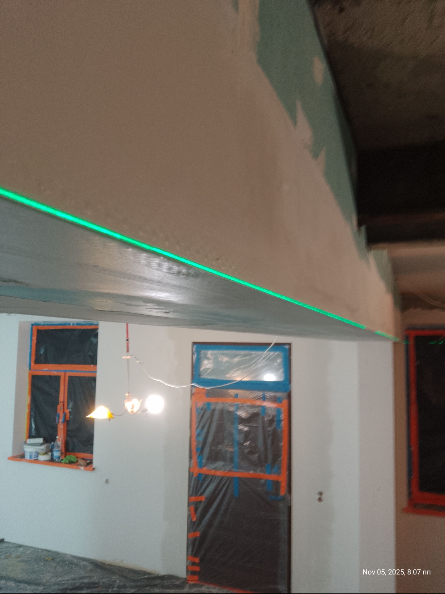 Wyrównywanie sufitu płytami gipsowymi z użyciem lasera. Okna i drzwi zabezpieczone folią. Widoczne niedoskonałości na łączeniach płyt.