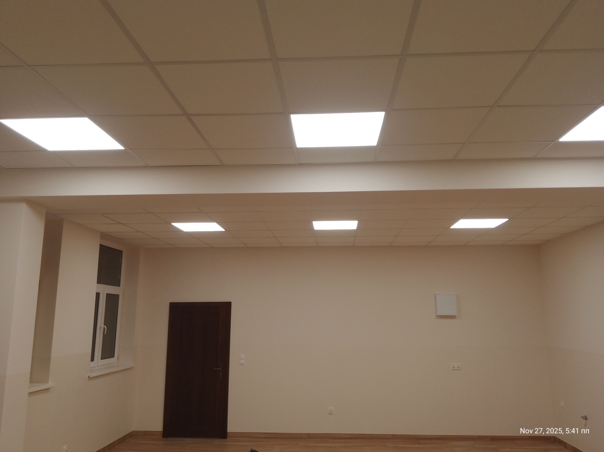 Zakończony montaż sufitu podwieszanego kasetonowego z oświetleniem LED w jasnym pomieszczeniu z oknem i drzwiami. Widoczna równa powierzchnia sufitu.