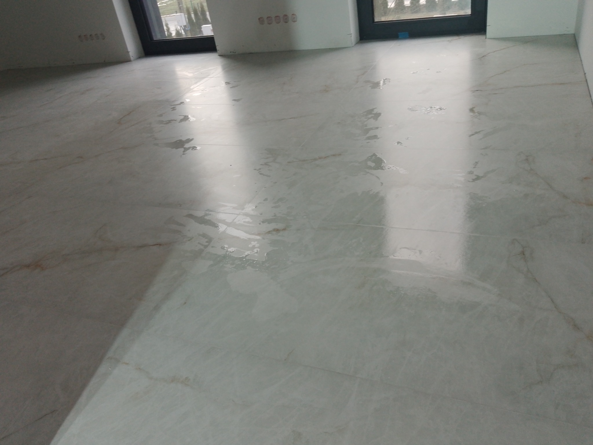 Błyszcząca, jasna podłoga z marmurowych płytek w nowym wnętrzu. Widoczne okna i fragmenty ścian. Świeżo położona podłoga z delikatnym wzorem.