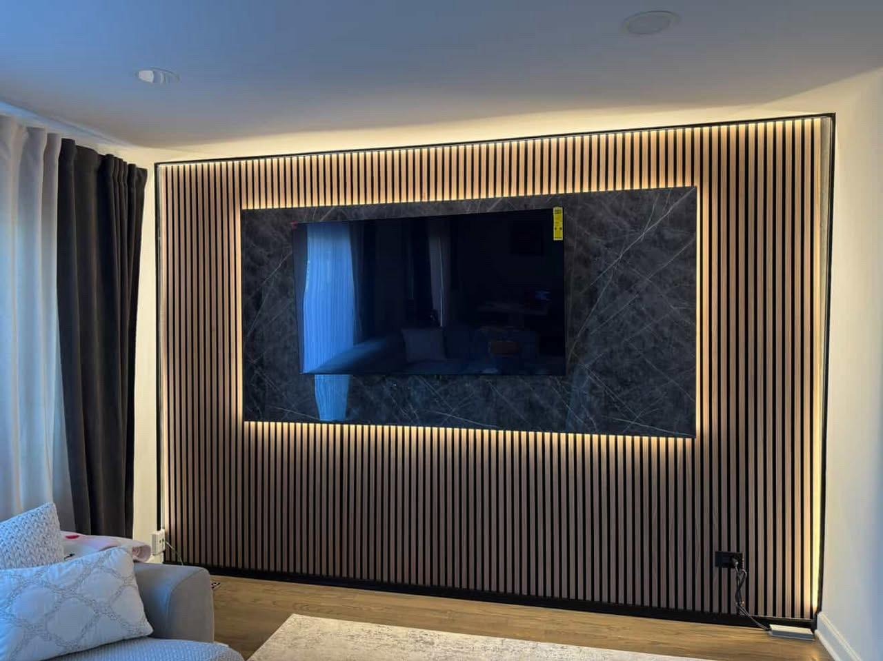 Ściana z paneli lamelowych z podświetleniem LED i marmurowym panelem za telewizorem. Nowoczesny design wnętrza salonu z zasłonami i częścią sofy.