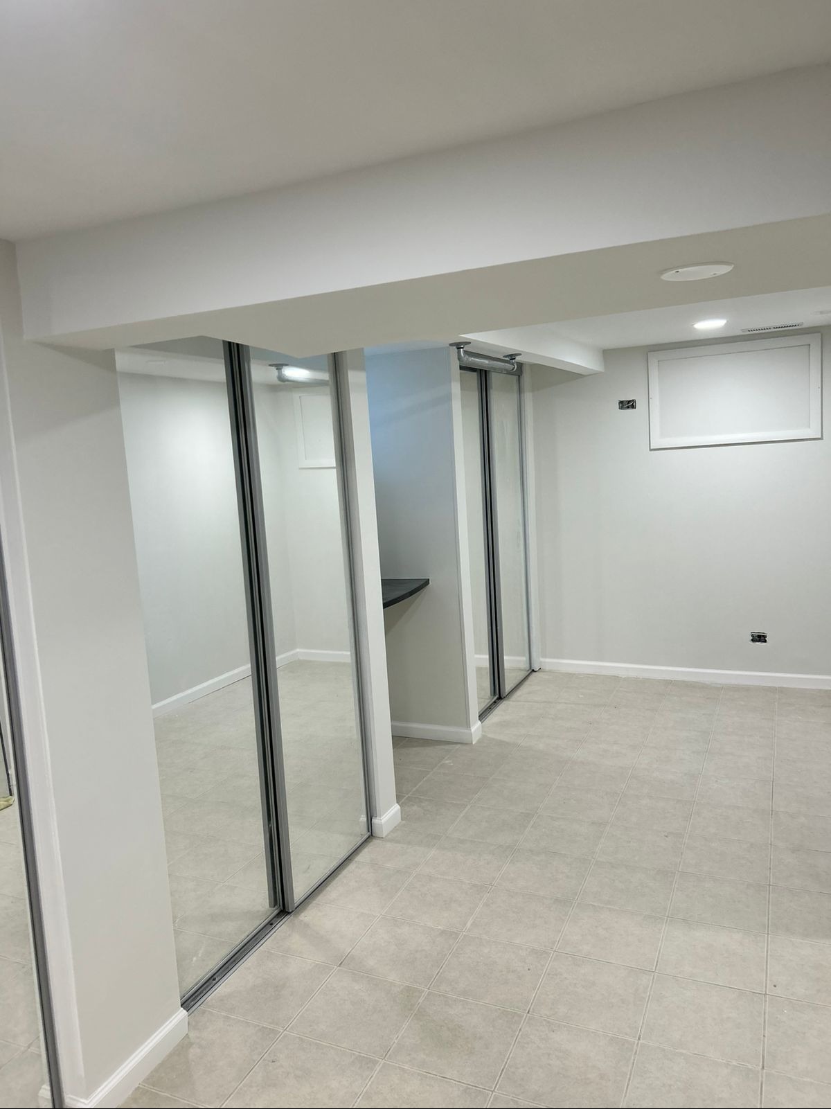 Jasne wnętrze z lustrzanymi drzwiami przesuwnymi i płytkami podłogowymi. Minimalistyczny design, świeżo po remoncie, z widocznym oświetleniem sufitowym i czystymi ścianami.