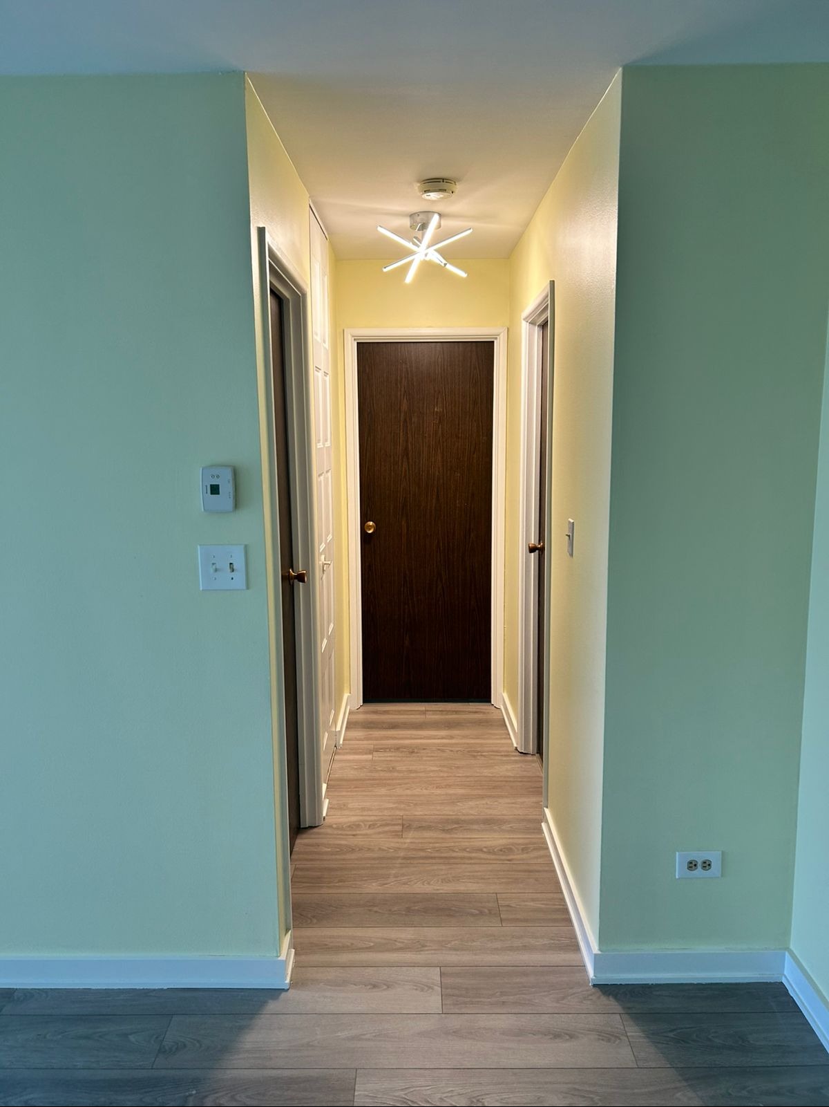 Wykończony korytarz w Godzieszach Wielkich z panelami podłogowymi, pomalowanymi ścianami na jasnozielono i żółto, oraz nowoczesną lampą sufitową w kształcie gwiazdy.