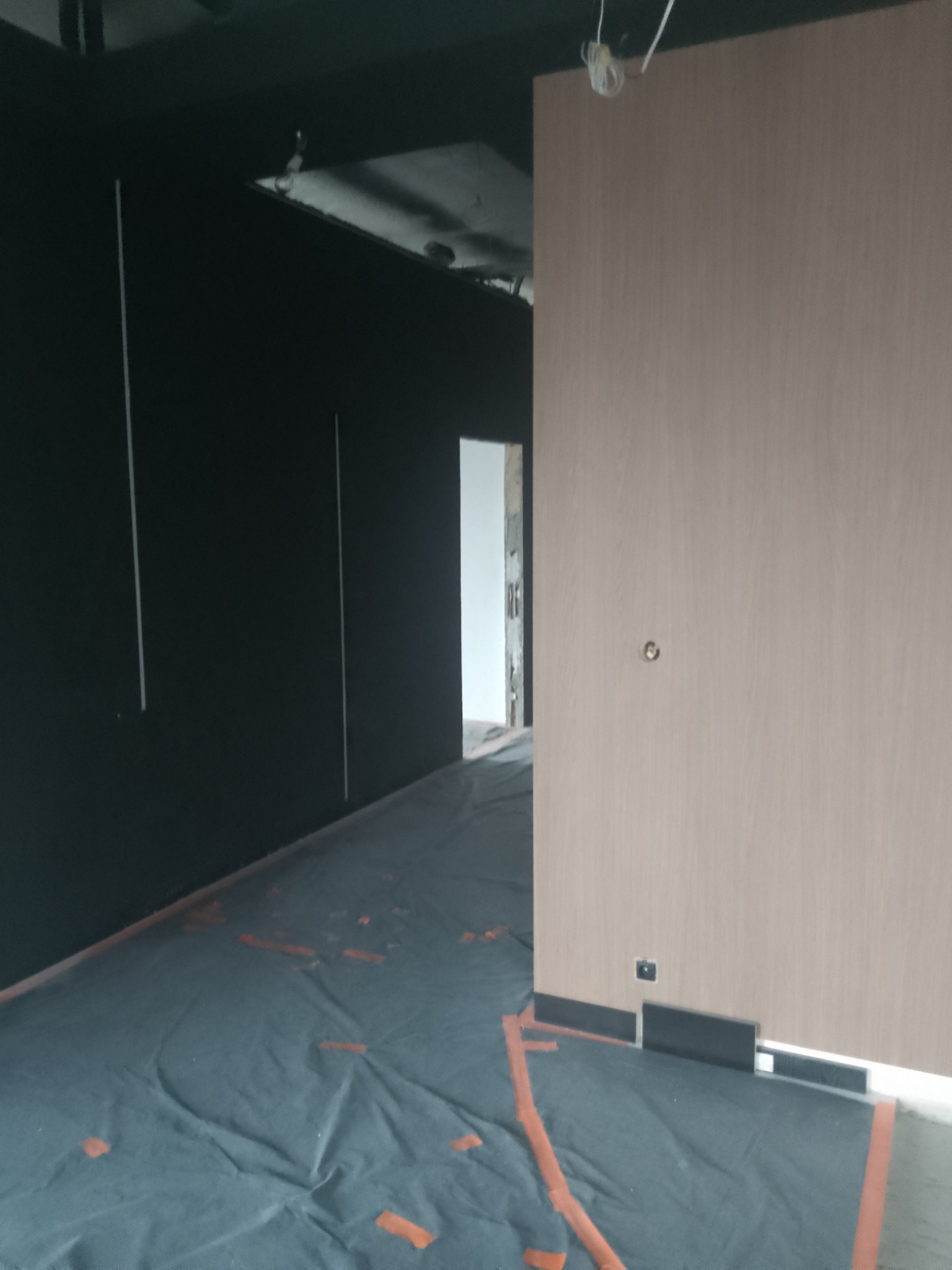 Ciemna ściana z pionowymi paskami i jasna ściana z zamontowanymi listwami przypodłogowymi. Podłoga zabezpieczona folią malarską. Wnętrze w trakcie wykańczania.