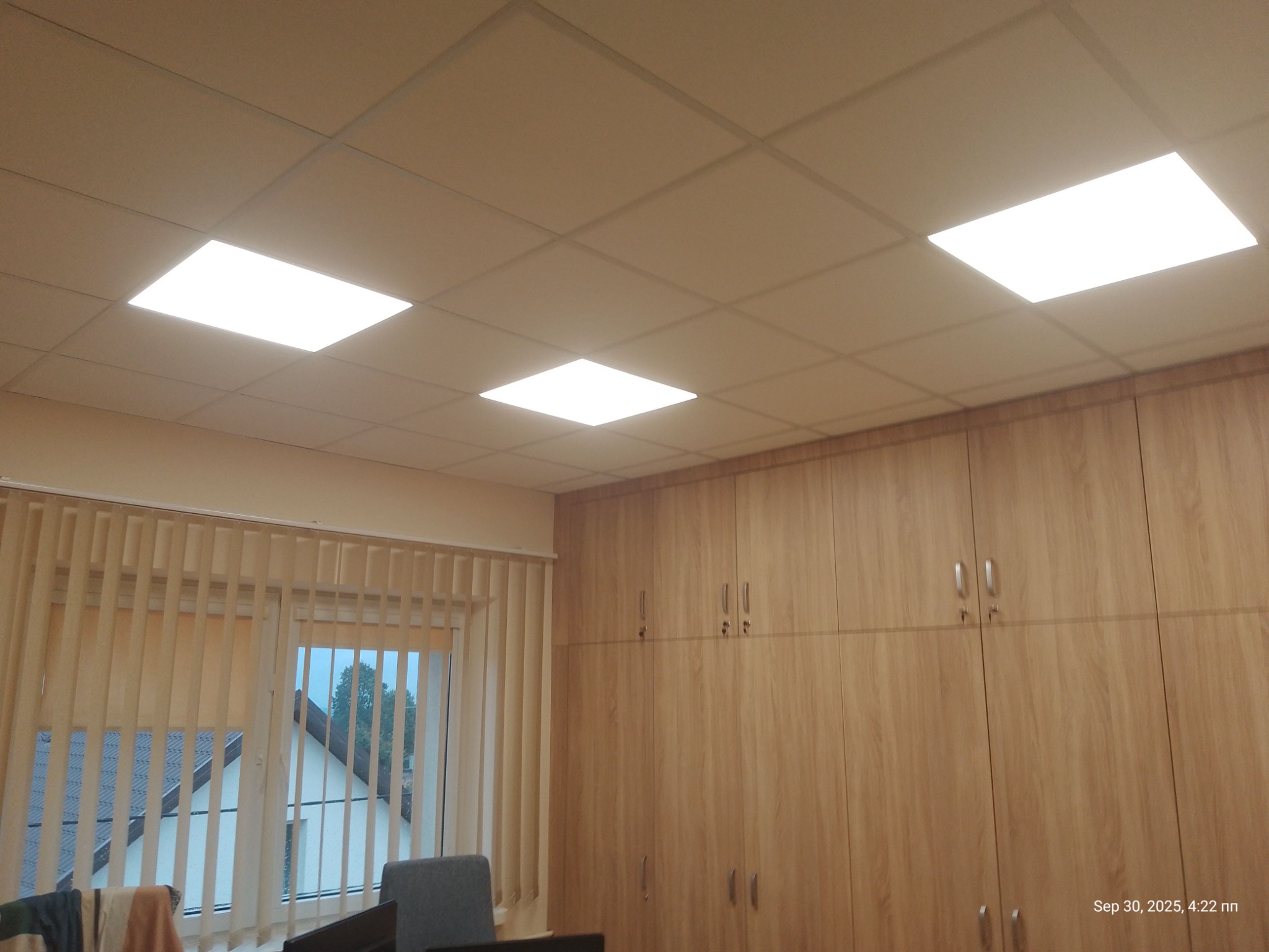 Sufit podwieszany z panelami LED w biurze w Godziesze Wielkie, widok z dołu. Jasne oświetlenie i drewniane szafy w tle.