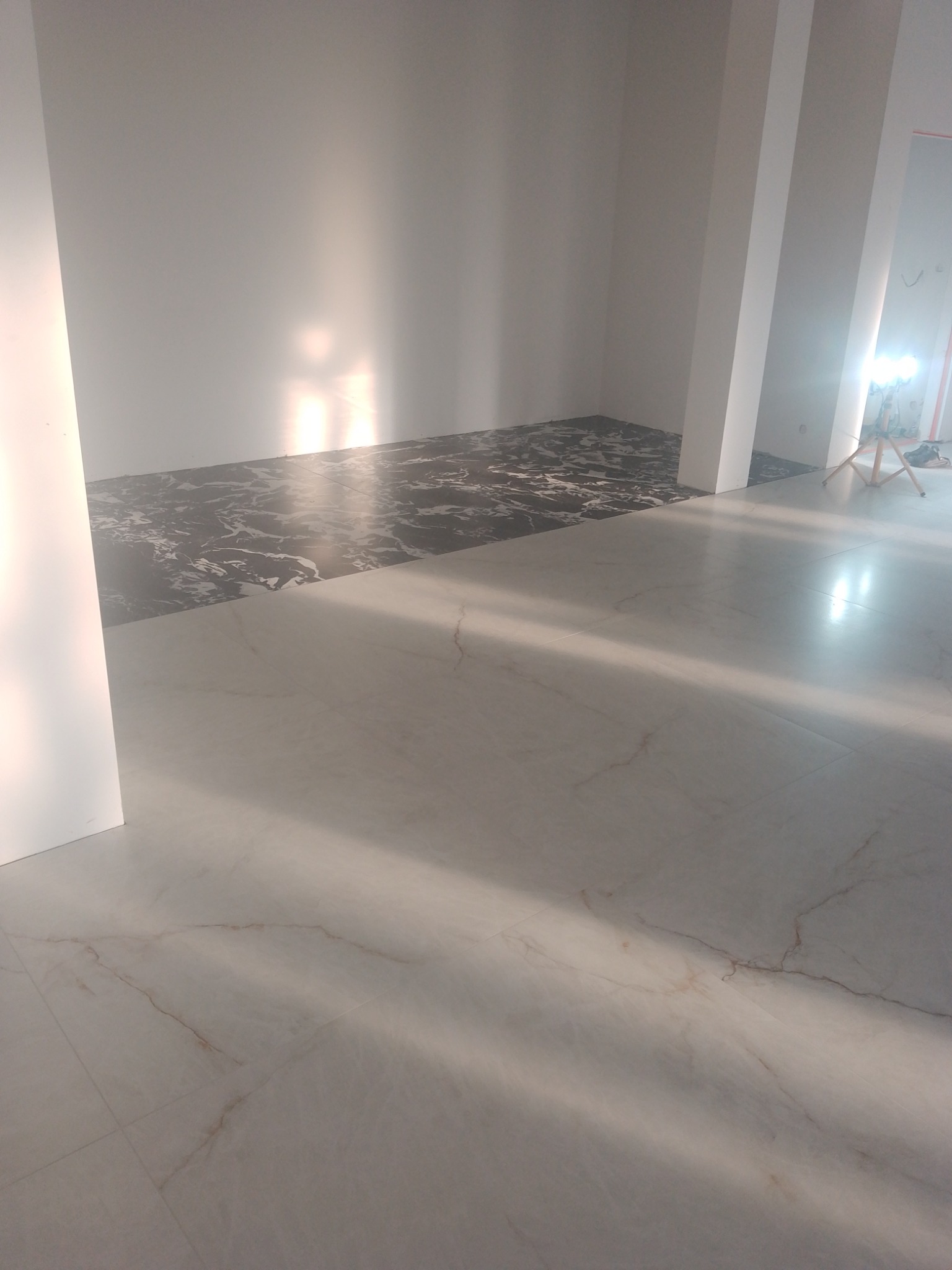Ukończona podłoga z płytek: jasne płytki imitujące marmur przechodzą w ciemne, wzorzyste płytki. Widoczne fragmenty ścian i kolumn w jasnym pomieszczeniu.