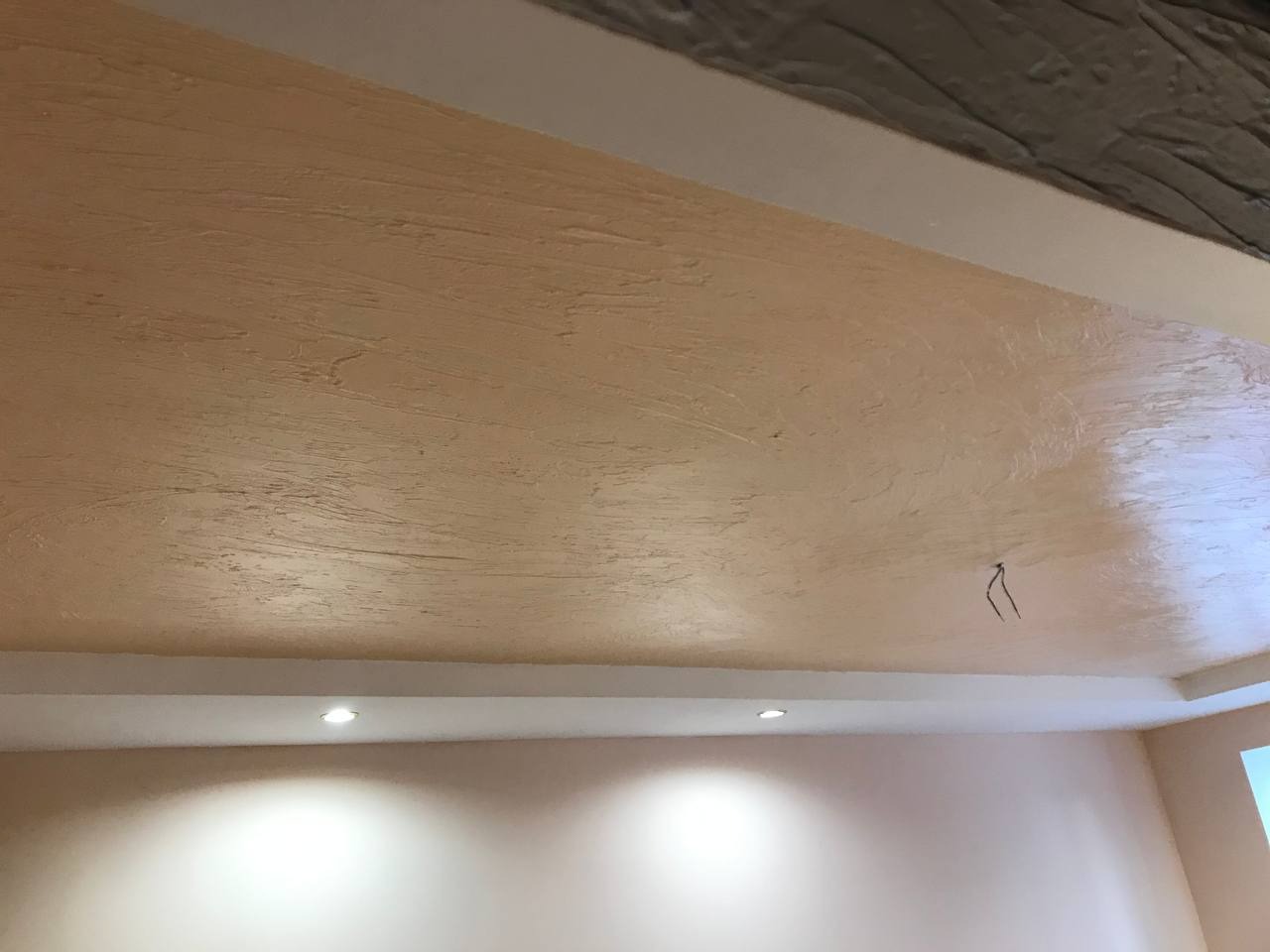 Beżowy sufit z fakturą dekoracyjną i oświetleniem punktowym, widok z dołu. Wykończenie wnętrza z efektem strukturalnym.