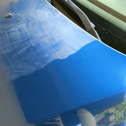 Studio Polerka - Fragment niebieskiej karoserii auta z widocznymi śladami polerowania, ukazujący różnicę w połysku przed i po zabiegu. W tle wycieraczka szyby.