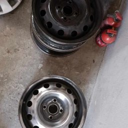 Studio Polerka - Stos felg stalowych, jedna czysta, inne czarne, obok kołpaki i gaśnice. Felgi po czyszczeniu prezentują się lepiej.