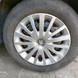 Koło samochodu marki Peugeot z srebrną felgą i oponą zimową na tle kostki brukowej. Widoczne detale bieżnika i oznaczenia opony.