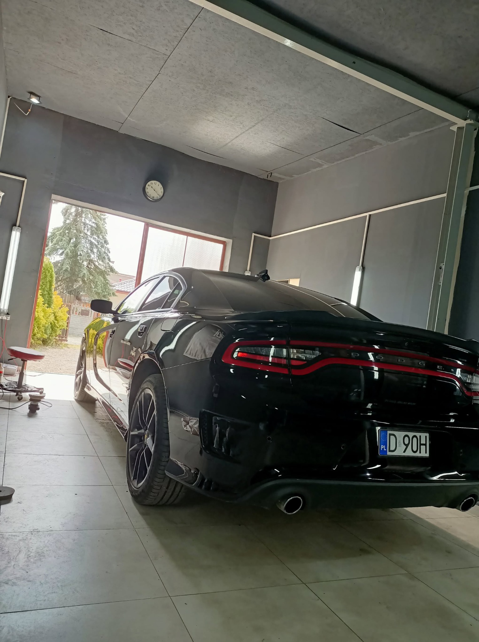 Błyszczący, czarny Dodge Charger po detailingu w myjni. Widok z tyłu, z widocznym numerem rejestracyjnym, w tle brama garażowa i zieleń.
