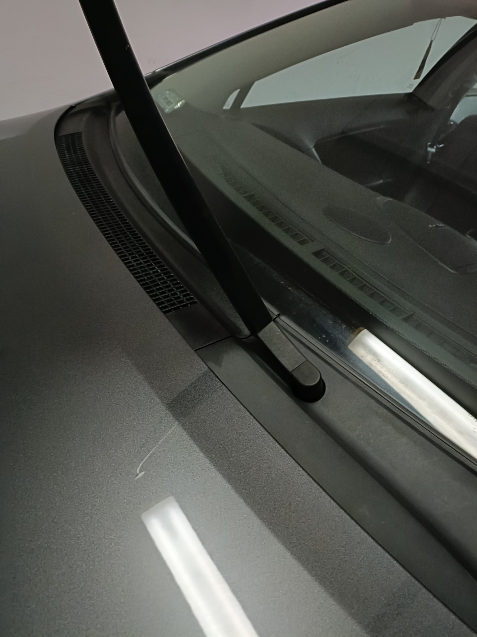 Szary samochód: wycieraczka, szyba i fragment karoserii z drobnym zarysowaniem. Widoczne detale wykończenia i faktura lakieru. Ujęcie z bliska.