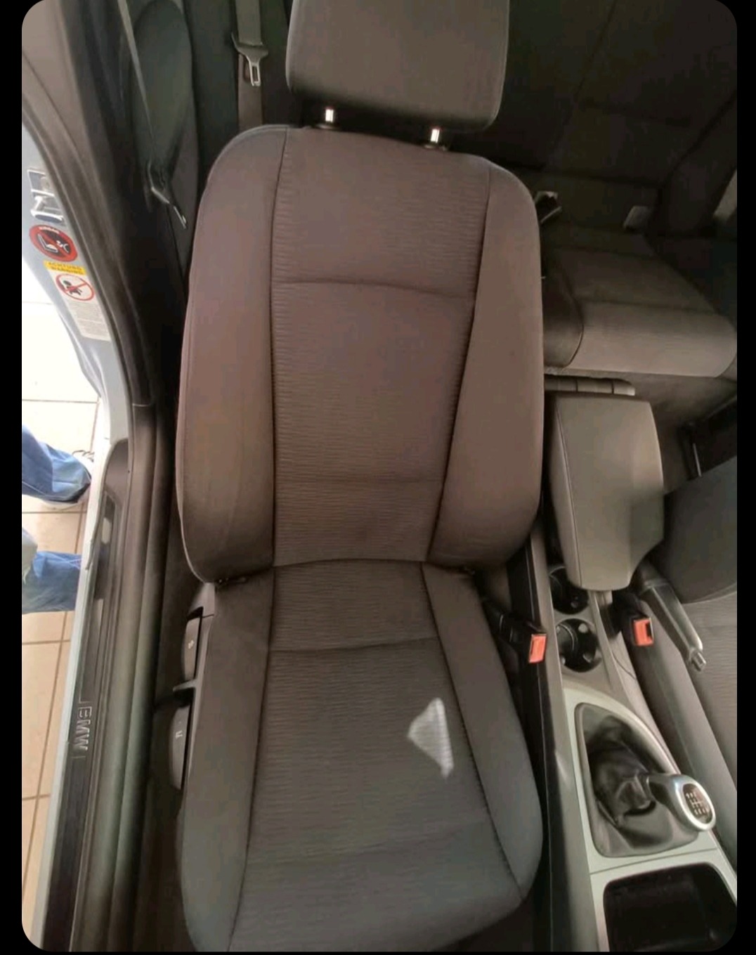 Wnętrze BMW z wypranym, szarym fotelem kierowcy. Widoczna dźwignia zmiany biegów i fragment deski rozdzielczej. Czysta tapicerka po usłudze.