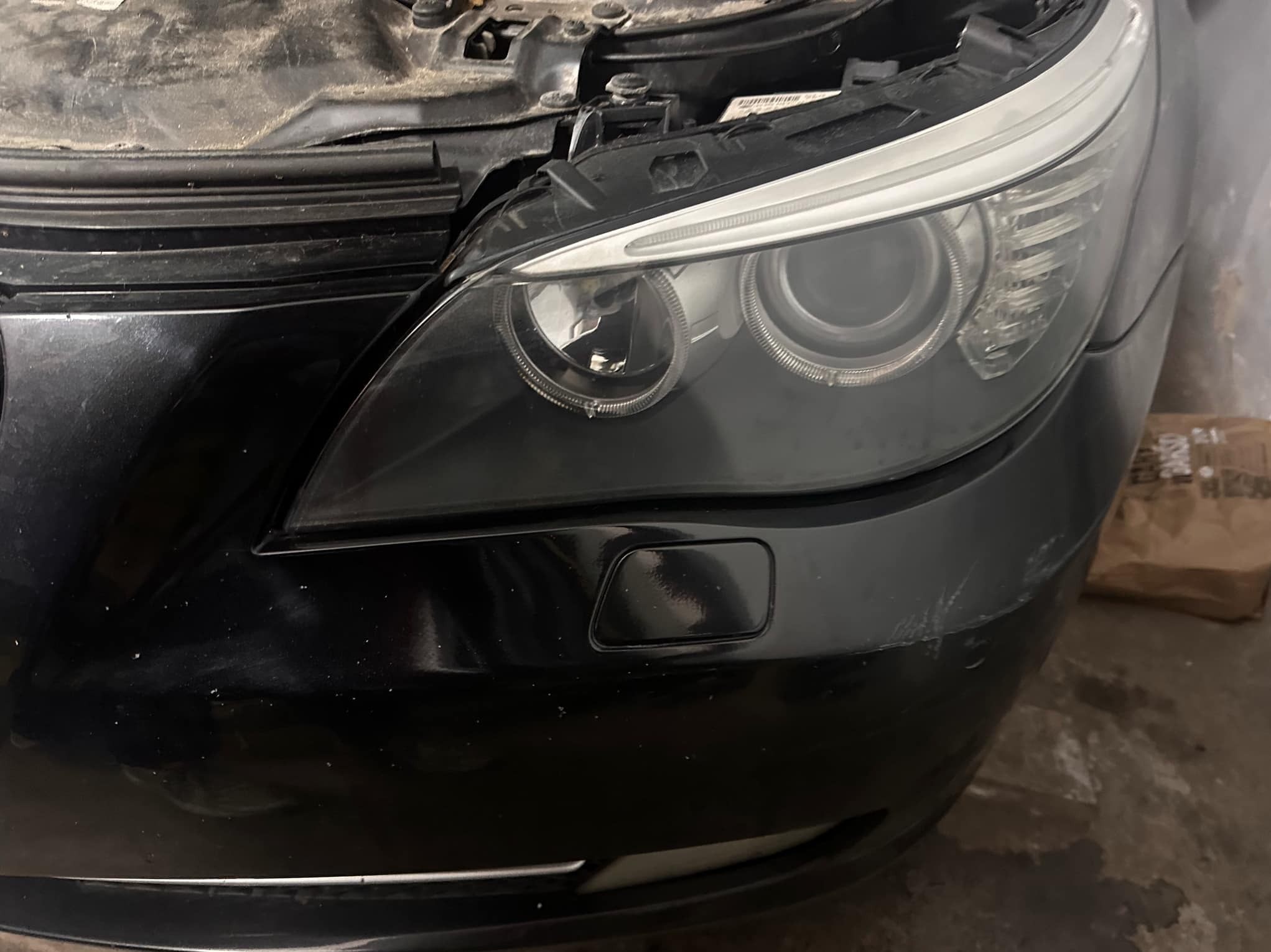Fragment czarnego samochodu z widocznym przednim reflektorem i zarysowaniami na zderzaku.  Widoczny brud na karoserii.
