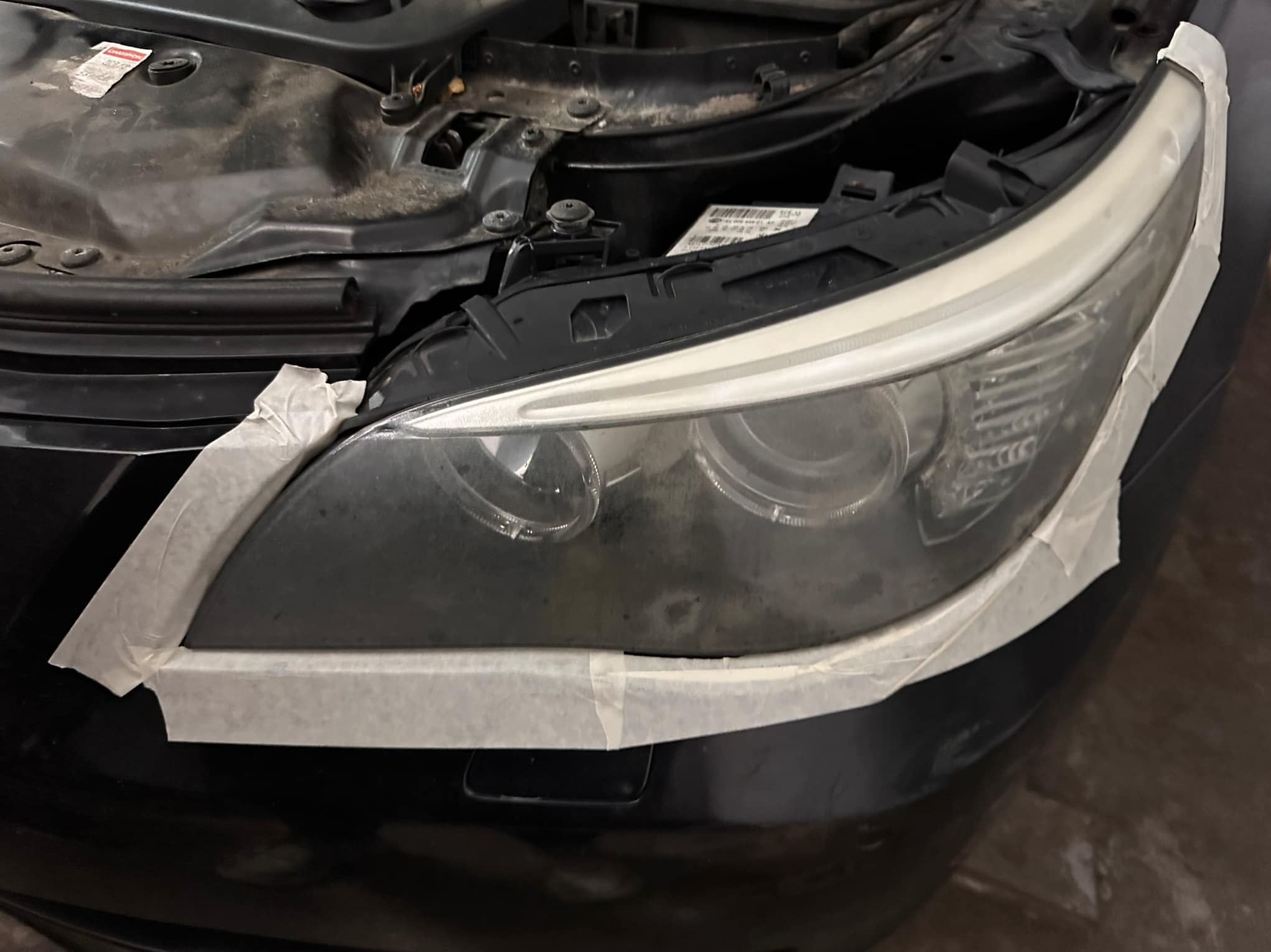 Reflektor samochodowy przed polerowaniem, zabezpieczony taśmą maskującą, widoczne zarysowania i zabrudzenia na kloszu. Detailing auta.