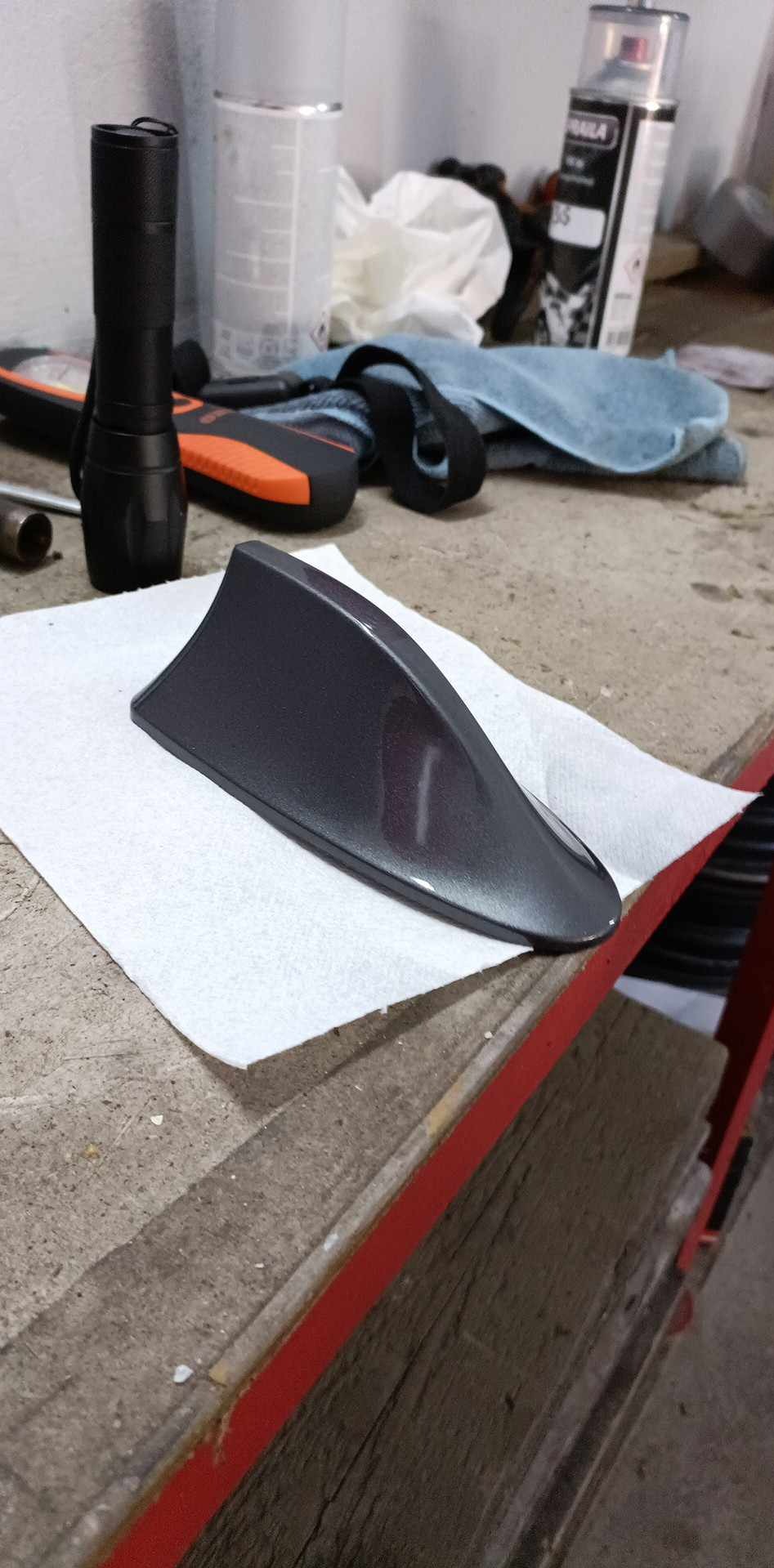 Pomalowana płetwa rekina na papierze, obok narzędzia i puszka farby. Detailing samochodowy, odnowa lakieru. Szary, błyszczący lakier.