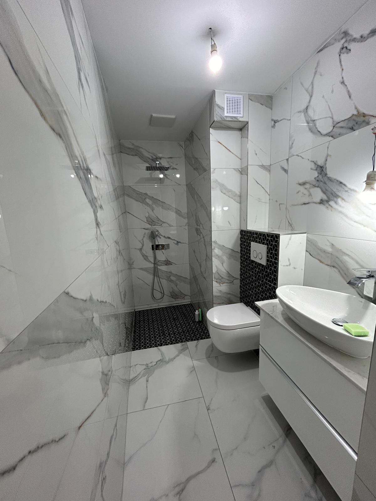 Nowoczesna łazienka z marmurowymi płytkami, kabiną prysznicową i umywalką nablatową. Kontrast czarnej mozaiki dodaje elegancji. Wykończenie wnętrz.