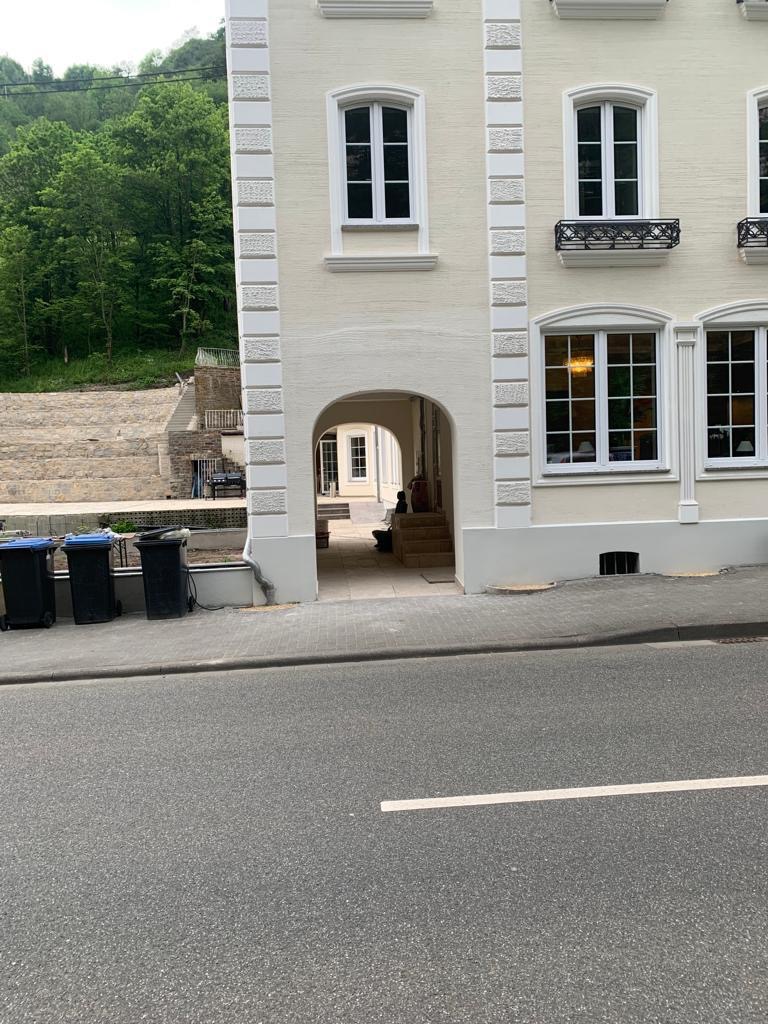 Elewacja budynku z białymi oknami i łukowym przejściem. Widoczne detale architektoniczne i otoczenie budynku. Ujęcie z poziomu ulicy, z widocznymi koszami.