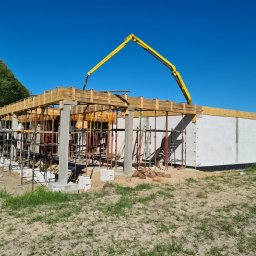 Wytwórnia Materiałów Budowlanych Zdzisława Szczepańska - Budowa domu jednorodzinnego w Sępólnie Krajeńskim w trakcie wylewania betonowych słupów i stropu przy użyciu pompy do betonu; widoczne szalunki i zbrojenia.