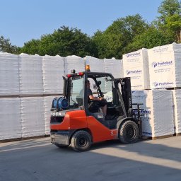 Wytwórnia Materiałów Budowlanych Zdzisława Szczepańska - Wózek widłowy Toyota przewozi palety z prefabrykatami betonowymi owiniętymi folią stretch na terenie składu, widoczne logo producenta Prefabet na opakowaniach.