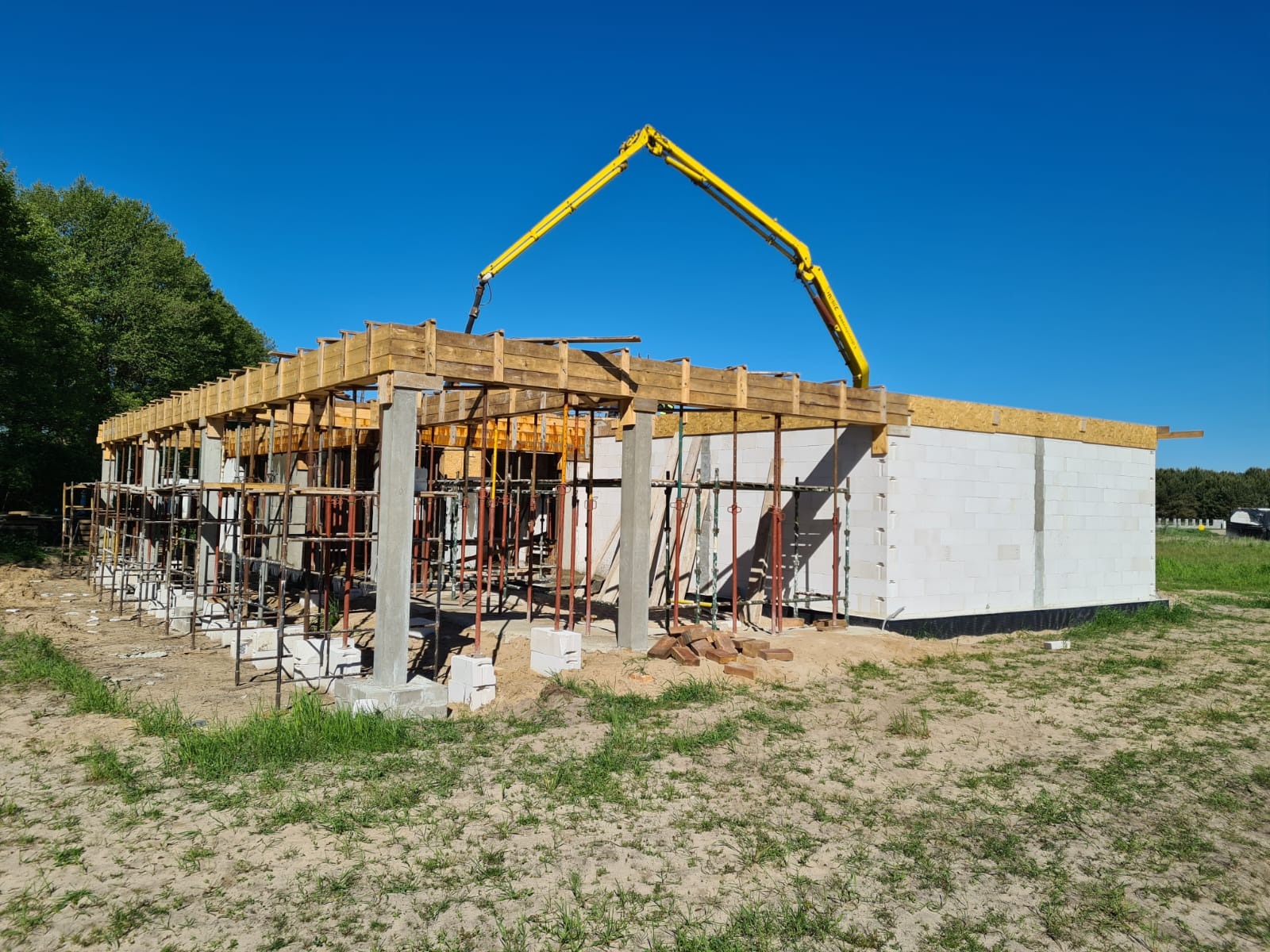 Budowa domu jednorodzinnego w Sępólnie Krajeńskim w trakcie wylewania betonowych słupów i stropu przy użyciu pompy do betonu; widoczne szalunki i zbrojenia.