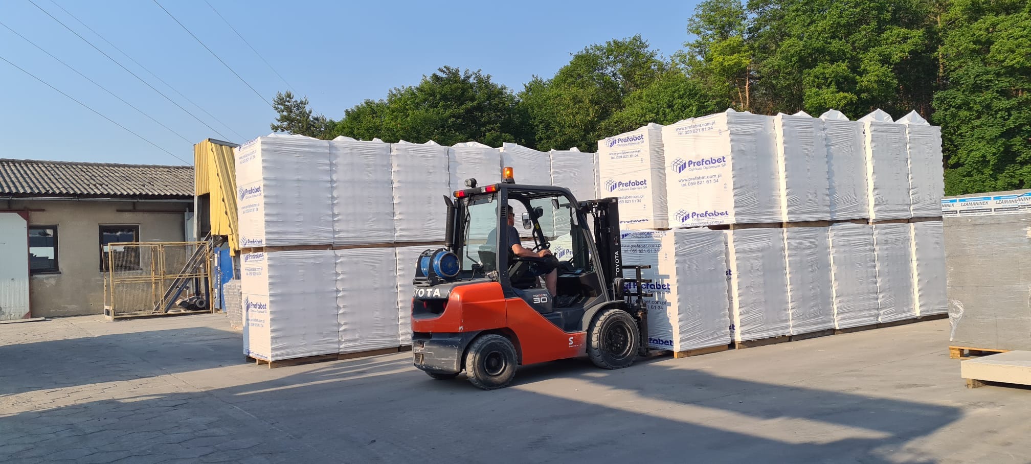 Wózek widłowy Toyota przewozi palety z prefabrykatami betonowymi owiniętymi folią stretch na terenie składu, widoczne logo producenta Prefabet na opakowaniach.