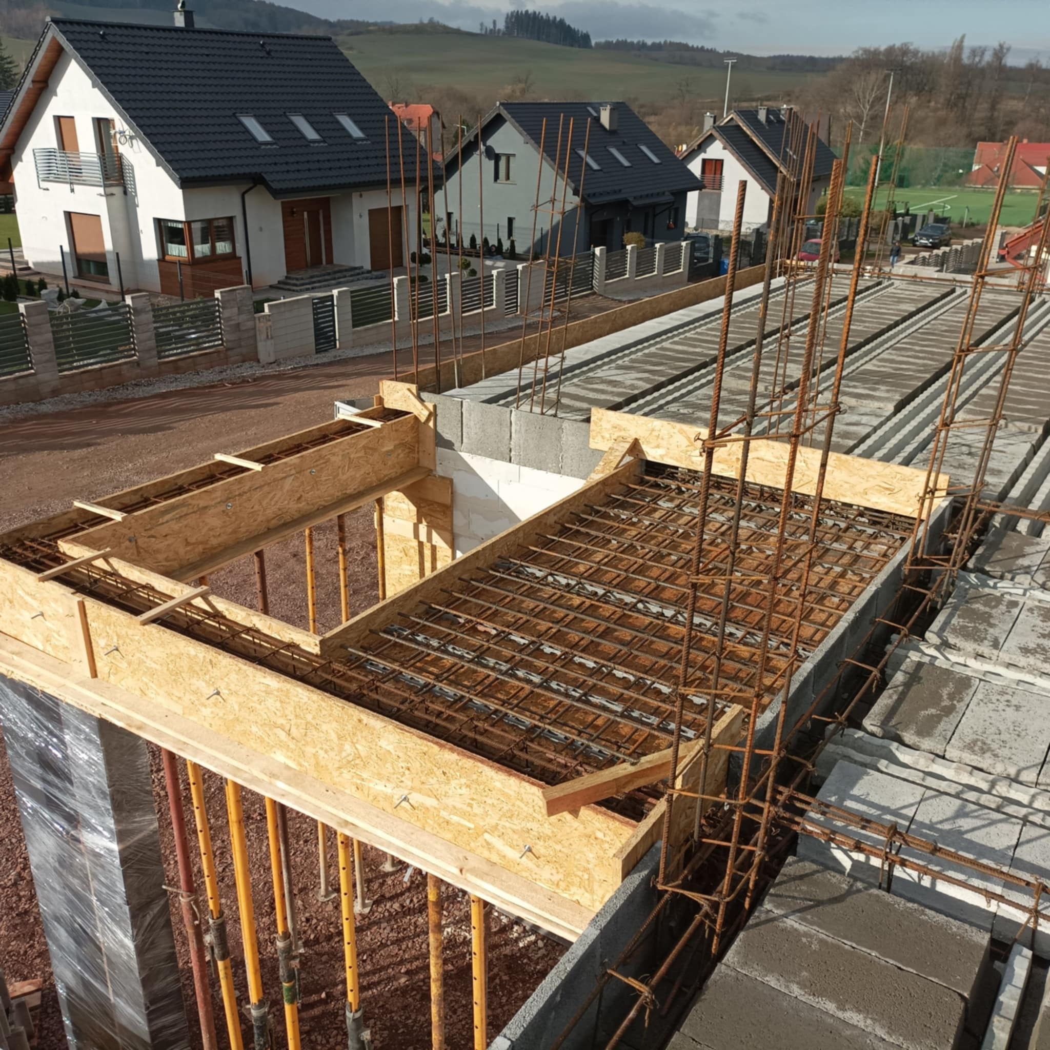 Budowa stropu Teriva: szalunki z płyty OSB, siatka zbrojeniowa, pustaki stropowe na tle zabudowy jednorodzinnej.