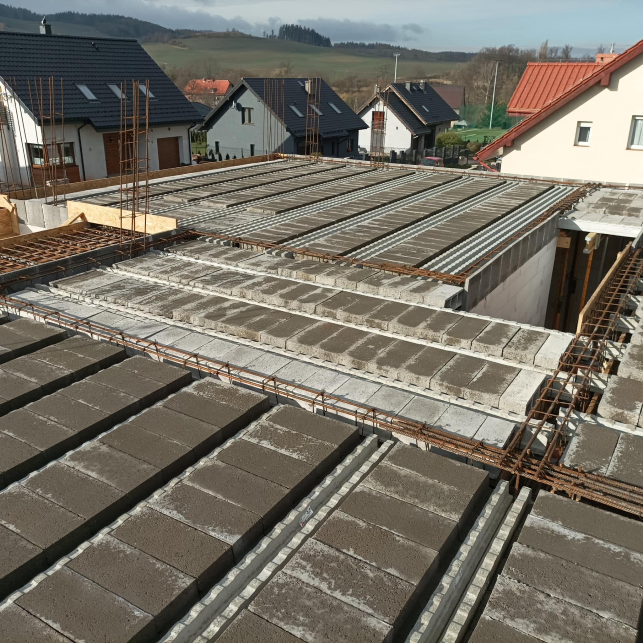 Budowa stropu Teriva z belek i pustaków, zbrojenie stalowe widoczne, domy jednorodzinne w tle, widok z góry.