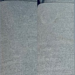 Pranie Tąpiecerki Clean_Service - Szara kanapa z widoczną różnicą w czystości tapicerki: po lewej stronie 'po' czyszczeniu, po prawej 'przed', z widocznymi plamami.