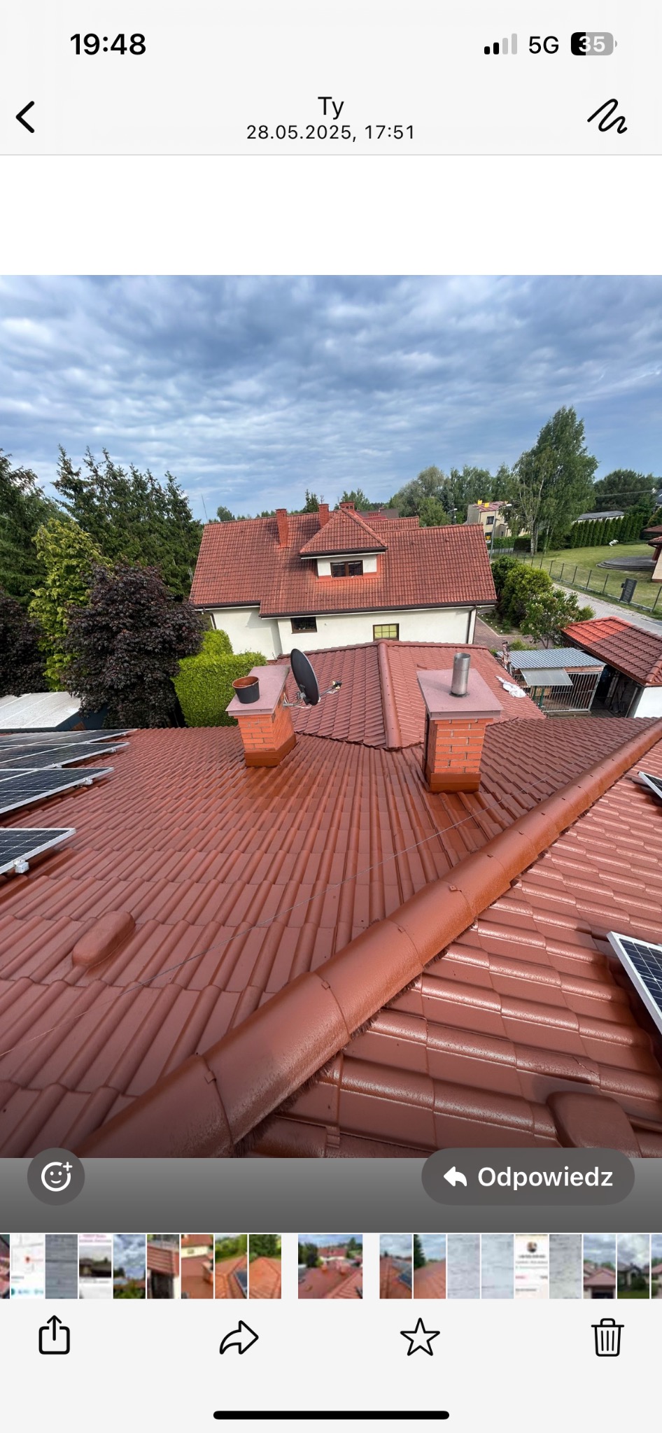 Czerwony dach z dachówki ceramicznej po renowacji, widok z góry. Dwa kominy z cegły, panele słoneczne i fragment rynny. W tle dom i zieleń drzew.